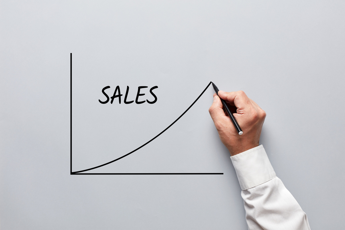 Male hand drawing a graph of sales on gray background. Increasing sales in business